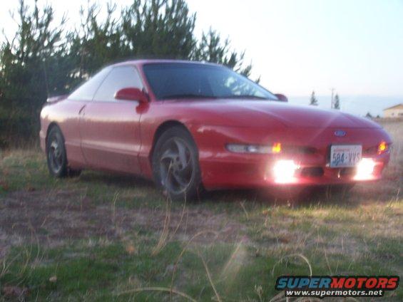 Red 1994 Ford Probe parked on grassy area with trees in background