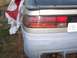 1994 Ford Probe - The rear of a gold car shows a damaged bumper and taillight assembly, partially obscured by a tarp.