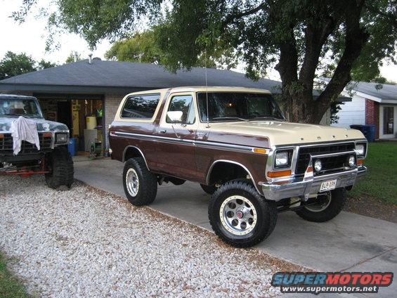 Lifted two-tone brown and tan Ford Bronco parked in a driveway next to another lifted truck