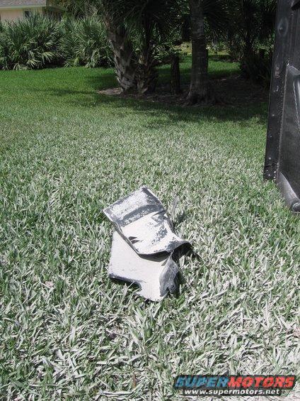 Bent and torn white and black car fender part on grass