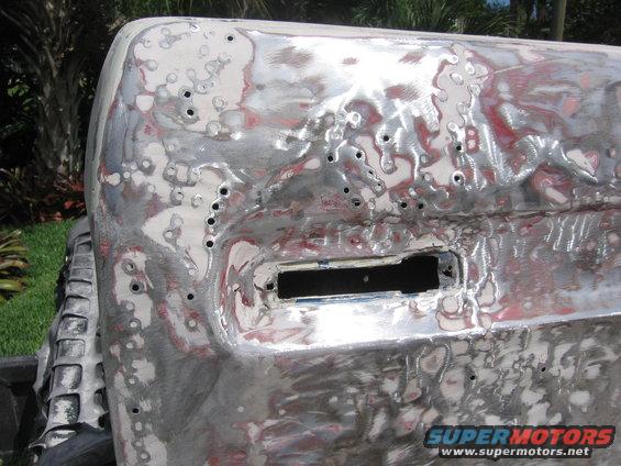 Close-up of a vehicle's metal body panel with primer and sanding marks, showing a rectangular cutout