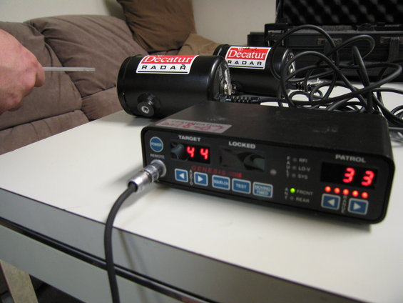 Two black Decatur radar units and a black Genesis I radar detector with red digital displays on a white table