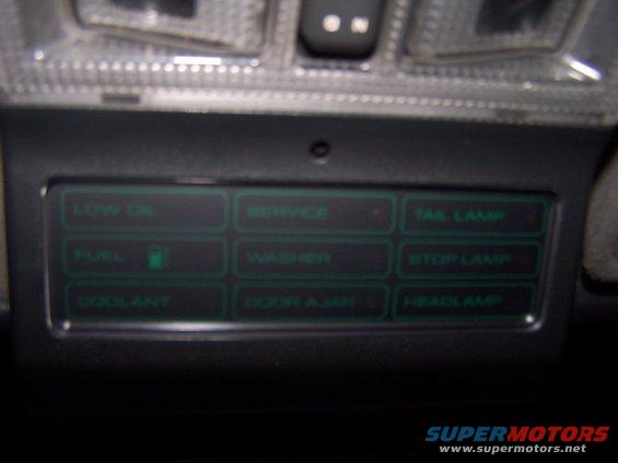 Dashboard with illuminated green warning lights for low oil, fuel, coolant, service, washer, door ajar, tail lamp, stop lamp, and headlamp