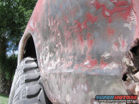 Side view of a red truck body with primer and sanding marks, showing a large tire
