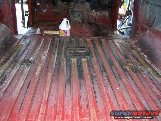 Red ribbed floor of a disassembled vehicle interior with a bottle of cleaner and a brush