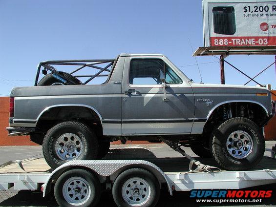 Gray and white Ford Bronco on a trailer, lifted with off-road tires and a roll cage