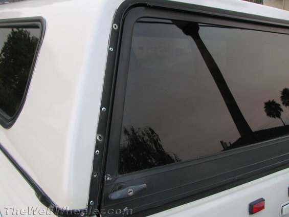 Close-up of a white truck cap with a tinted window and a black trim strip held by rivets