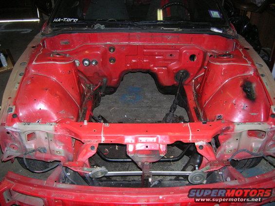 Red car engine bay, missing engine. Some parts removed. Sticker on windshield says HA-Toro