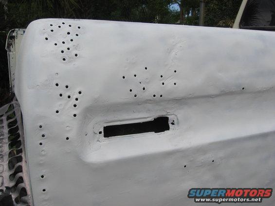 close-up of a white primed vehicle body panel with many small holes and a rectangular cutout