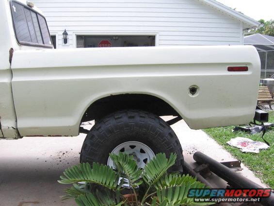 White pickup truck bed, side view, showing rust on lower body panel and large off-road tire