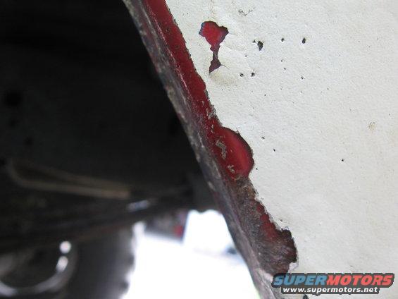 Close-up of a white painted metal edge with red showing through rust and peeling paint, likely a wheel well