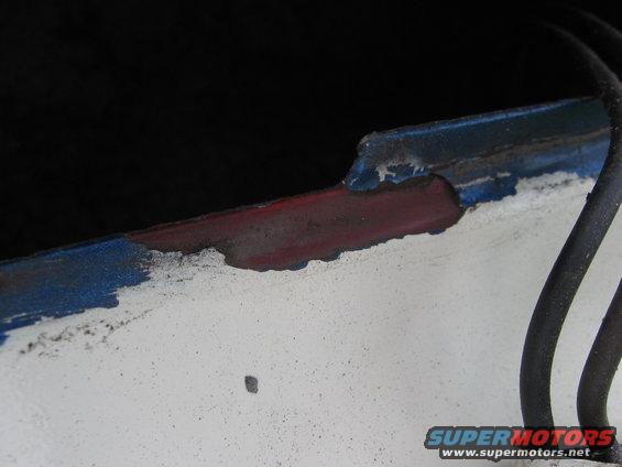 Close-up of chipped blue and red paint on a white vehicle edge, showing rust underneath. A black wire is visible