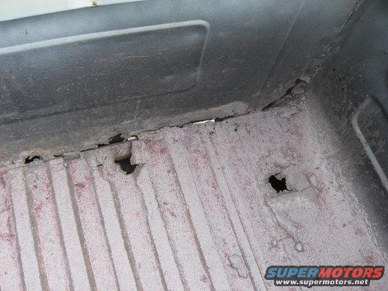 Corroded truck bed floor with holes and red undercoating