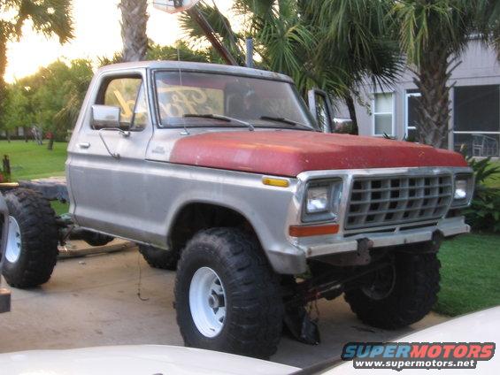 Silver pickup truck with red hood, large tires, and no rear bed