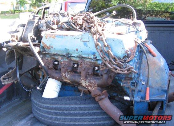 Rusted blue engine block with chains, resting on a tire in a truck bed