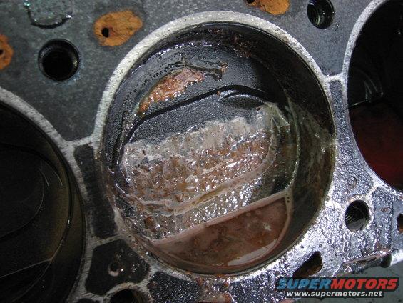 Engine cylinder block showing rust and sludge buildup inside one cylinder