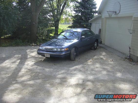 Dark blue sedan parked in a driveway next to a garage. License plate is visible