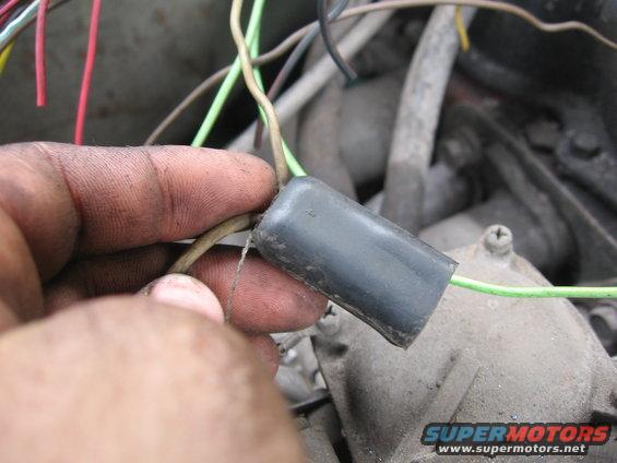 Close-up of a hand holding a wiring harness connector with green and tan wires