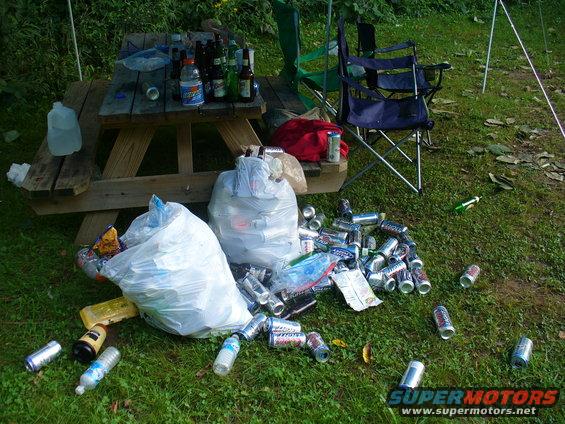 Picnic table covered in bottles and cans, with trash bags and scattered aluminum cans on the grass