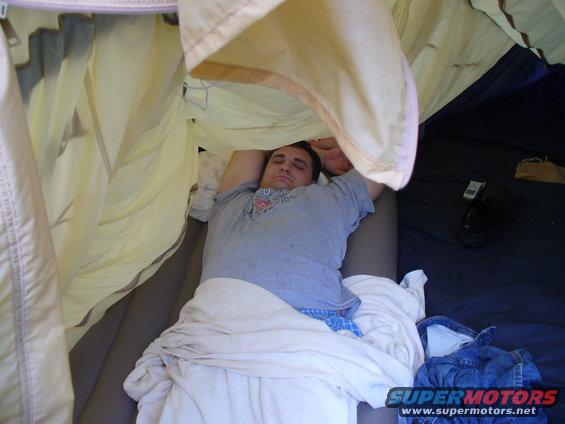 Man sleeping on an air mattress inside a tent, with blue jeans and a phone visible