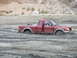 1987 Ford Bronco - A red pickup truck is stuck in thick mud, with its doors open and wheels submerged.