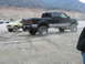 1987 Ford Bronco - Two pickup trucks are parked in a dusty, outdoor environment with mountains in the background.