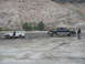 1987 Ford Bronco - Two off-road vehicles are stuck in a muddy area with a rocky hillside in the background.