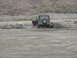 1987 Ford Bronco - Two vehicles are stuck in a sandy area with a rocky hillside in the background.