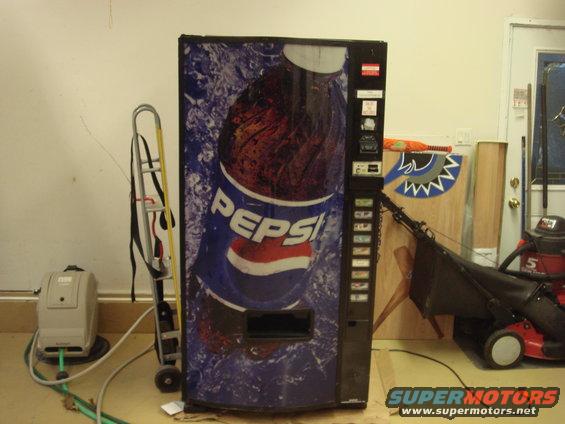 Pepsi vending machine in a garage with a lawnmower and dolly