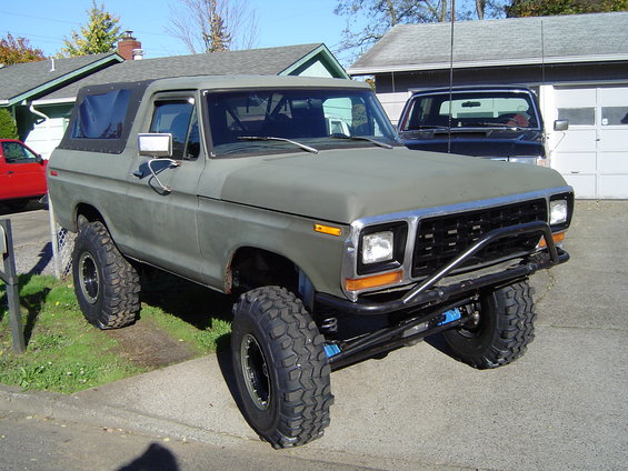 Olive green 1978 Ford Bronco with off-road tires and brush guard, parked in driveway