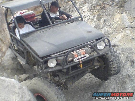 Buggy with two people driving over rocks. Has a winch on the front