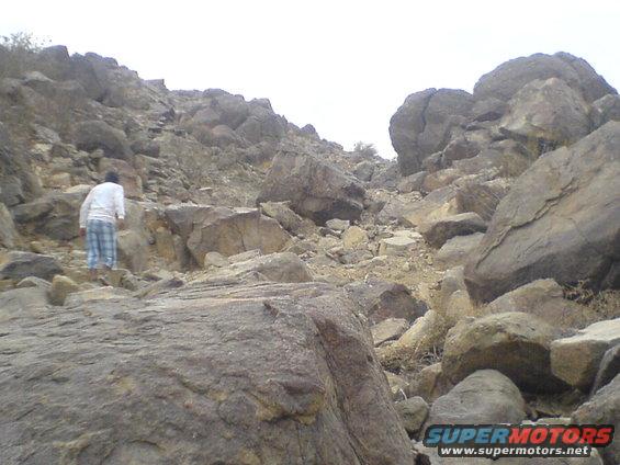 Person in plaid pants and white shirt climbing a steep, rocky slope