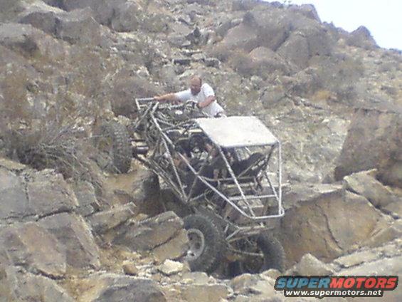 Off-road buggy with a roll cage climbing a rocky incline, driver visible