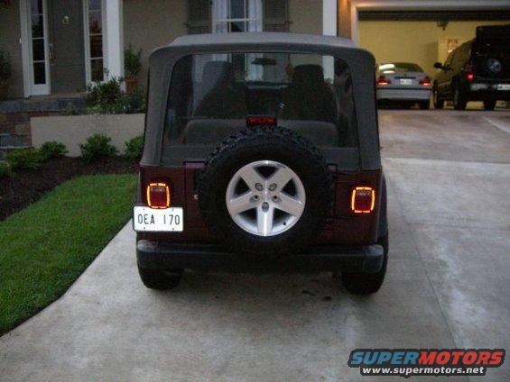 Maroon Jeep Wrangler with a spare tire on the rear, parked on a concrete driveway