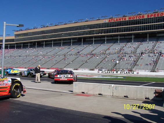 Race cars lined up on a track with grandstands in the background