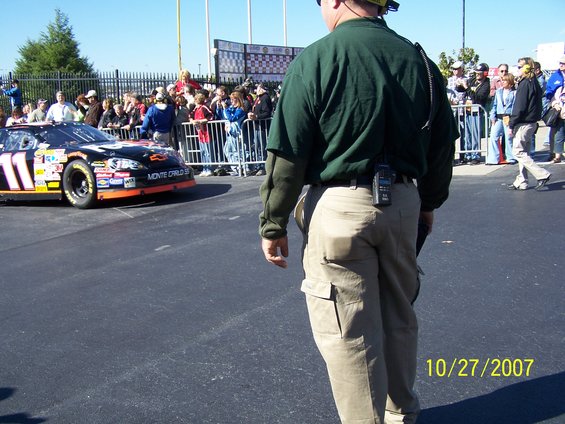 NASCAR race car with number 11 and 'MONTE CARLO SS' text, seen from the side with a crowd behind a fence