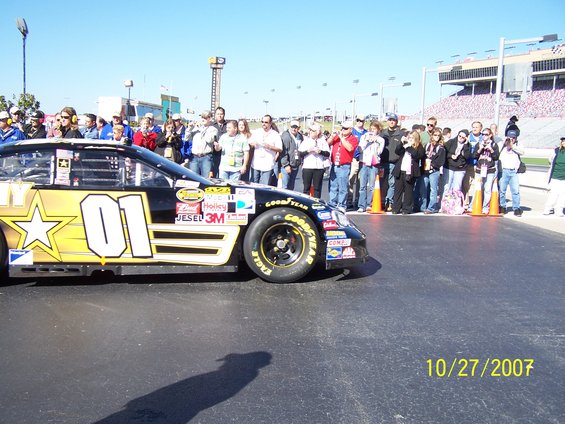 Race car with number 01 and a gold star on the side, parked on a track with spectators watching