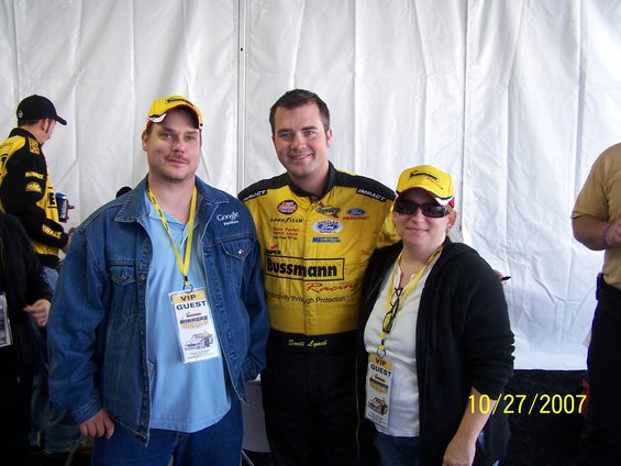 Three people in racing attire with VIP passes stand in front of a white tent, with a date stamp of 10/27/2007