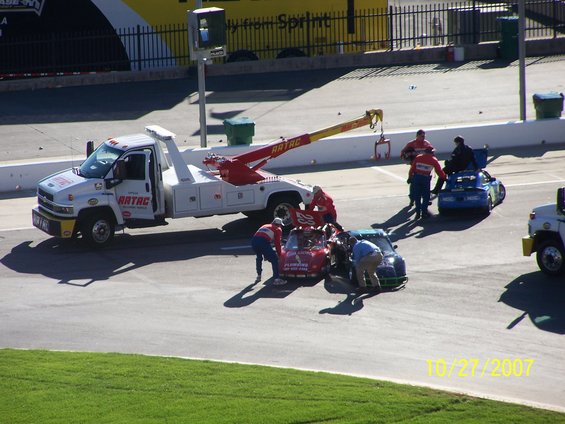 Tow truck and crew attending to a damaged race car on a track