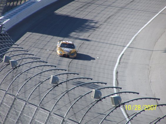 Gold race car with white and red accents on a track, seen from above