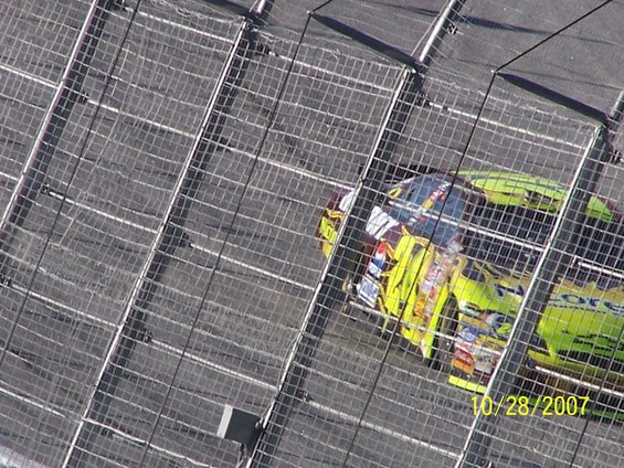 Two NASCAR race cars, one yellow and one green, on a track behind a fence. Date 10/28/2007 visible