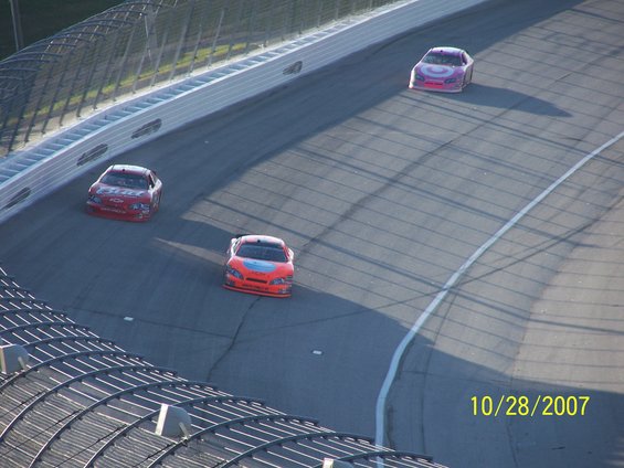 Three stock cars race on a track; one orange, one red, one purple. Date 10/28/2007 visible