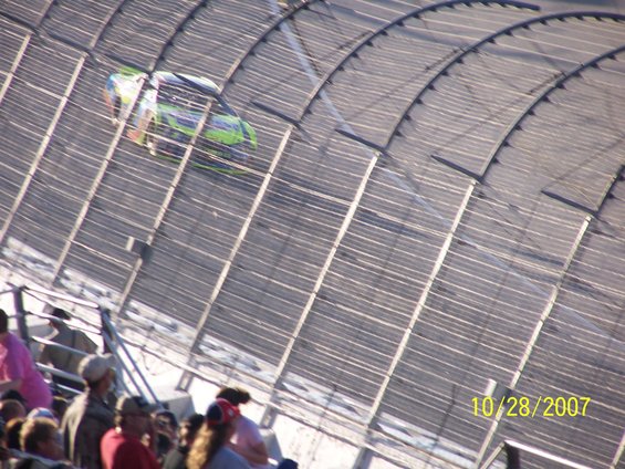 Race car with green and black paint scheme on a track, seen from above the stands. Date stamp 10/28/2007