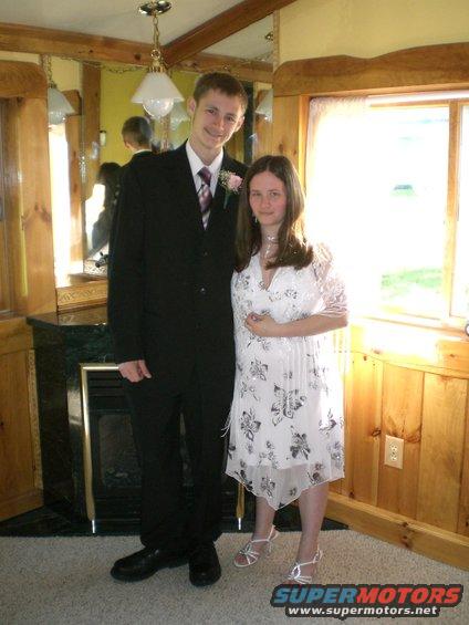Young man in a suit and young woman in a dress pose for a photo indoors