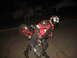 2007 Yamaha R1 - A person in full motorcycle gear performs a wheelie on a red bicycle under the cover of darkness.