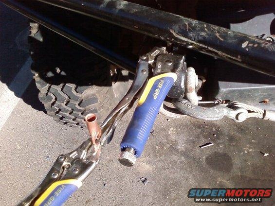 Vice grips holding a copper tube near a vehicle's tire and frame