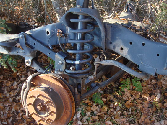 Rusty brake rotor and front suspension components of a vehicle, lying on the ground covered in leaves