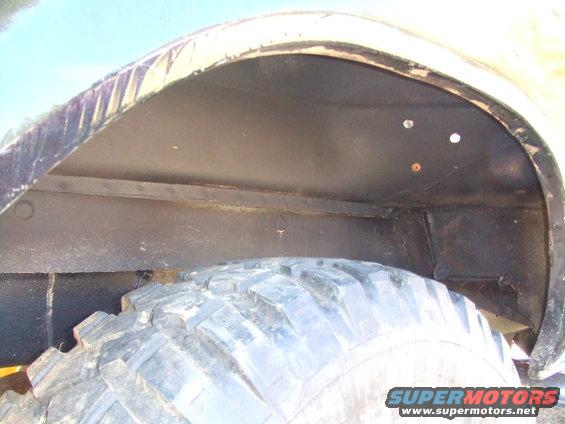 Wheel well interior with a large tire, showing black undercoating and some rust spots