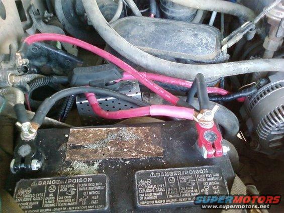 Engine bay with battery and pink cables. Text on battery reads DANGER/POISON