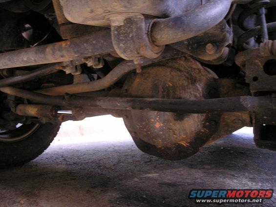 Undercarriage view of a vehicle's front differential and suspension components, with visible rust and dirt